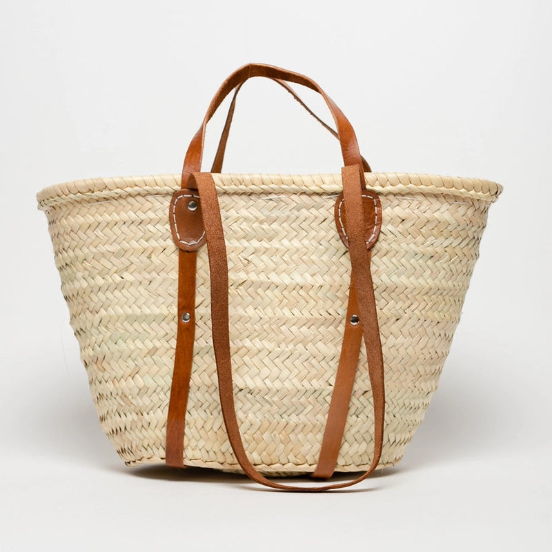Woven straw tote bag with brown leather straps on a white background